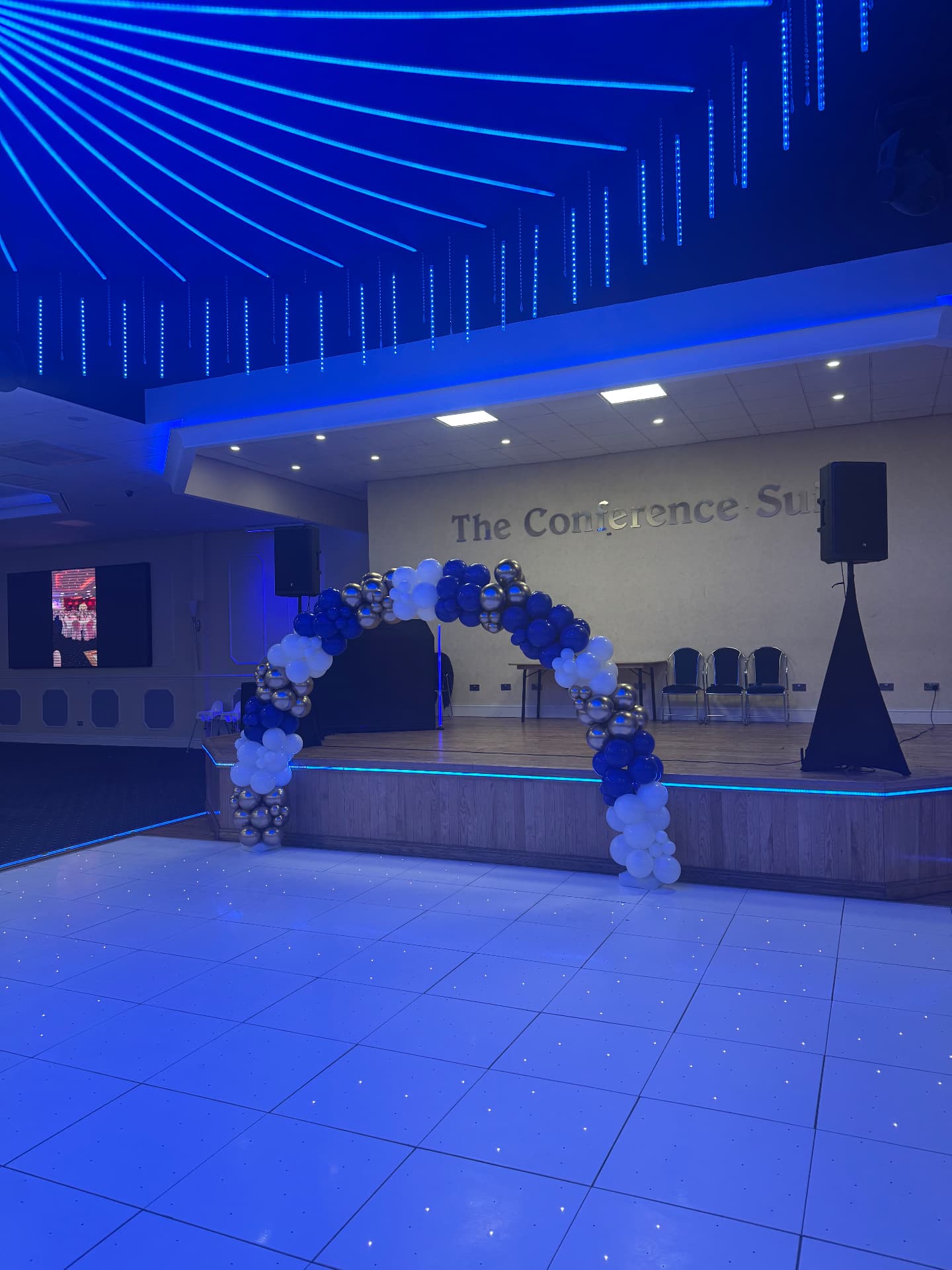 Venue dressed with blue uplighting, laser beams and a balloon arch by the DJ booth